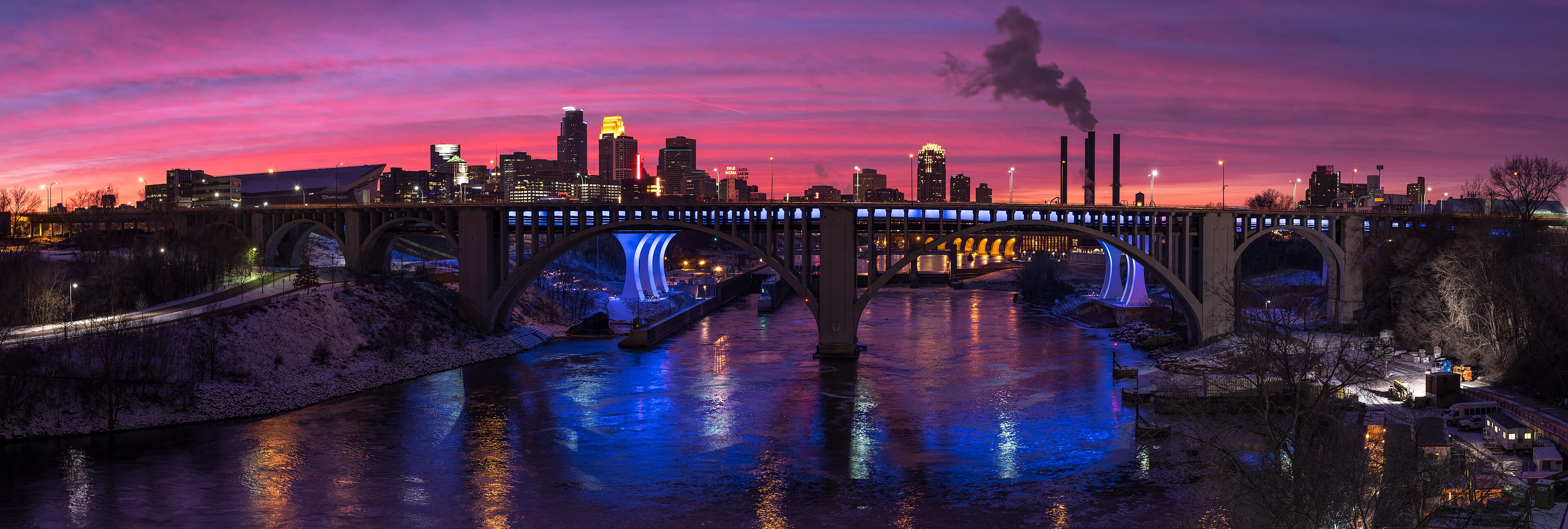 Authentic evening panorama of Minneapolis skyline over the Mississippi River, with illuminated bridges and pink dusk sky